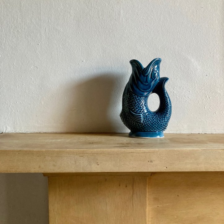 A teal gurgle (fish) jug from 1970s on a wooden mantelshelf.